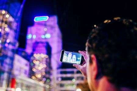 Eine männliche Person hält ein Smartphone hoch, um die am Abend bestrahlten Gebäude von Jenoptik zu fotografieren