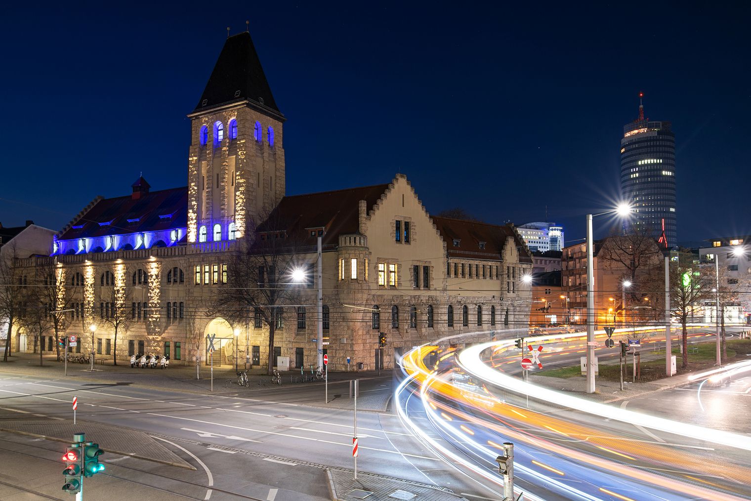 Eine Straßenbahn fährt schnell am Volksbad Jena vorbei, sodass ihre Lichter verschwimmen